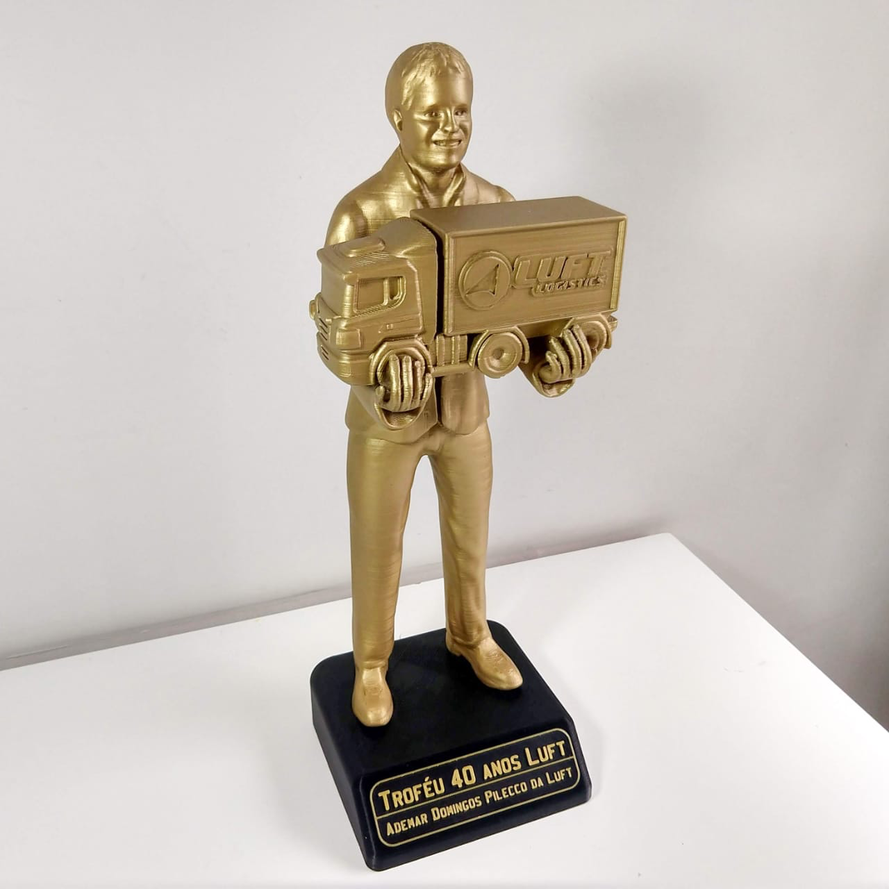 Troféu de resina dourada com a figura de um homem segurando um caminhão da Luft Logistics, sobre base preta com placa gravada