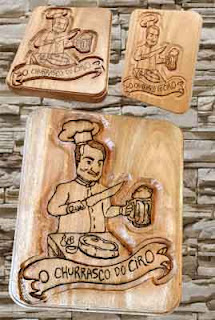 Placa de cedro em formato de tábua com a figura de um churrasqueiro em alto relevo e detalhes escurecidos com pirografia, com o texto "O Churrasco do Ciro"