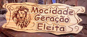 Placa horizontal de madeira pinus com bordas orgânicas, cabeça de leão pirografada e o texto "Mocidade Geração Eleita" entalhado