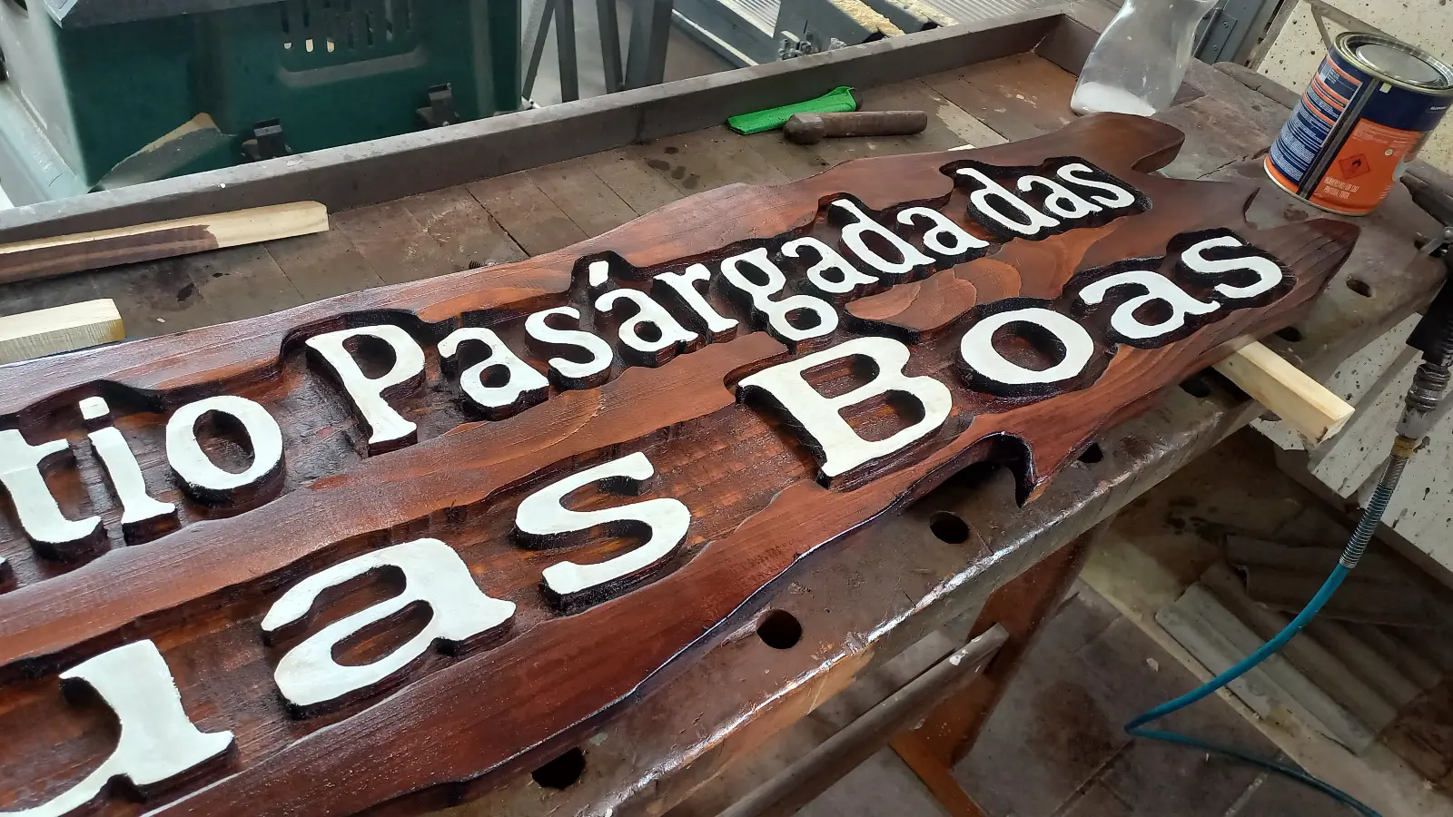 Detalhe em perspectiva da placa Sitio Pasargada das Boas Aguas com letras brancas em alto relevo sobre madeira tonalizada em nogueira na bancada de marcenaria