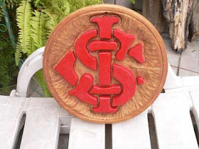 Brasão redondo de time de futebol entalhado em madeira de lei, com o escudo em alto relevo pintado de vermelho e fundo com textura radial