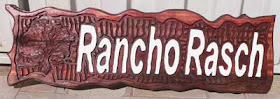 Placa horizontal de pinus com bordas orgânicas e o texto "Rancho Rasch" entalhado em alto relevo e pintado de branco