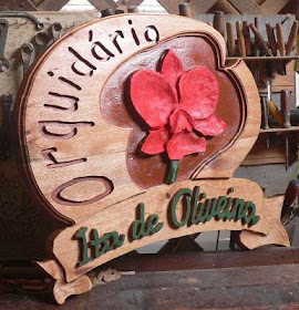 Placa de cedro branco em formato de coração com orquídea vermelha esculpida em alto relevo, a palavra "Orquidário" em baixo relevo e o nome "Ita de Oliveira" em faixa esculpida