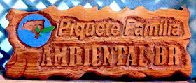 Placa de cedro branco com a logomarca pintada e o texto "Piquete Família Ambiental BR" entalhado em altíssimo alto relevo