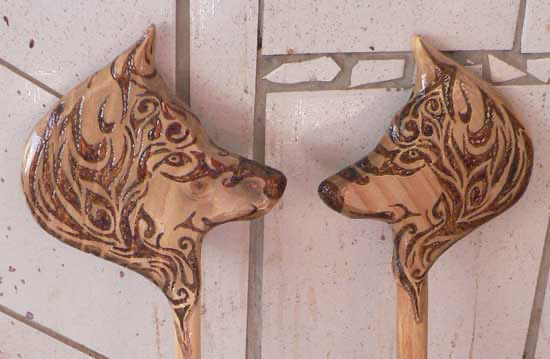 Duas peças de madeira recortadas em forma de cabeça de lobo, decoradas com desenhos tribais em pirografia