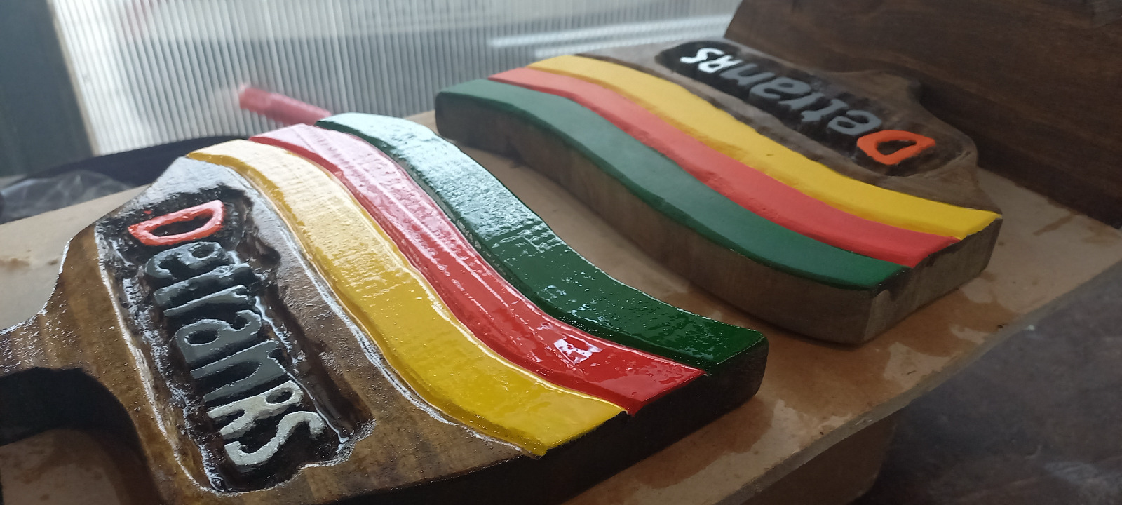 Detalhe aproximado de dois troféus em madeira maciça do DETRAN RS mostrando as faixas da bandeira em alto relevo e as letras esculpidas e pintadas à mão