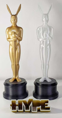 Duas estatuetas iguais de resina, uma dourada e uma branca, com orelhas longas, ao lado do logotipo Hype em relevo