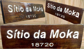Composição com três ângulos da placa de madeira escurecida com o texto "Sítio da Moka 18720" em letras brancas em baixo relevo