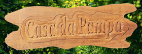 Placa de madeira em tonalidade natural com o texto "Casa da Pampa" entalhado em letras cursivas de alto relevo