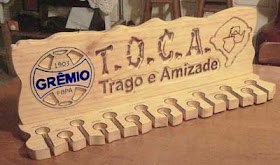 Porta espetos de madeira maciça de pinus com o brasão do Grêmio pintado, o mapa do Rio Grande do Sul pirografado e a frase "T.O.C.A., Trago e Amizade" entalhada