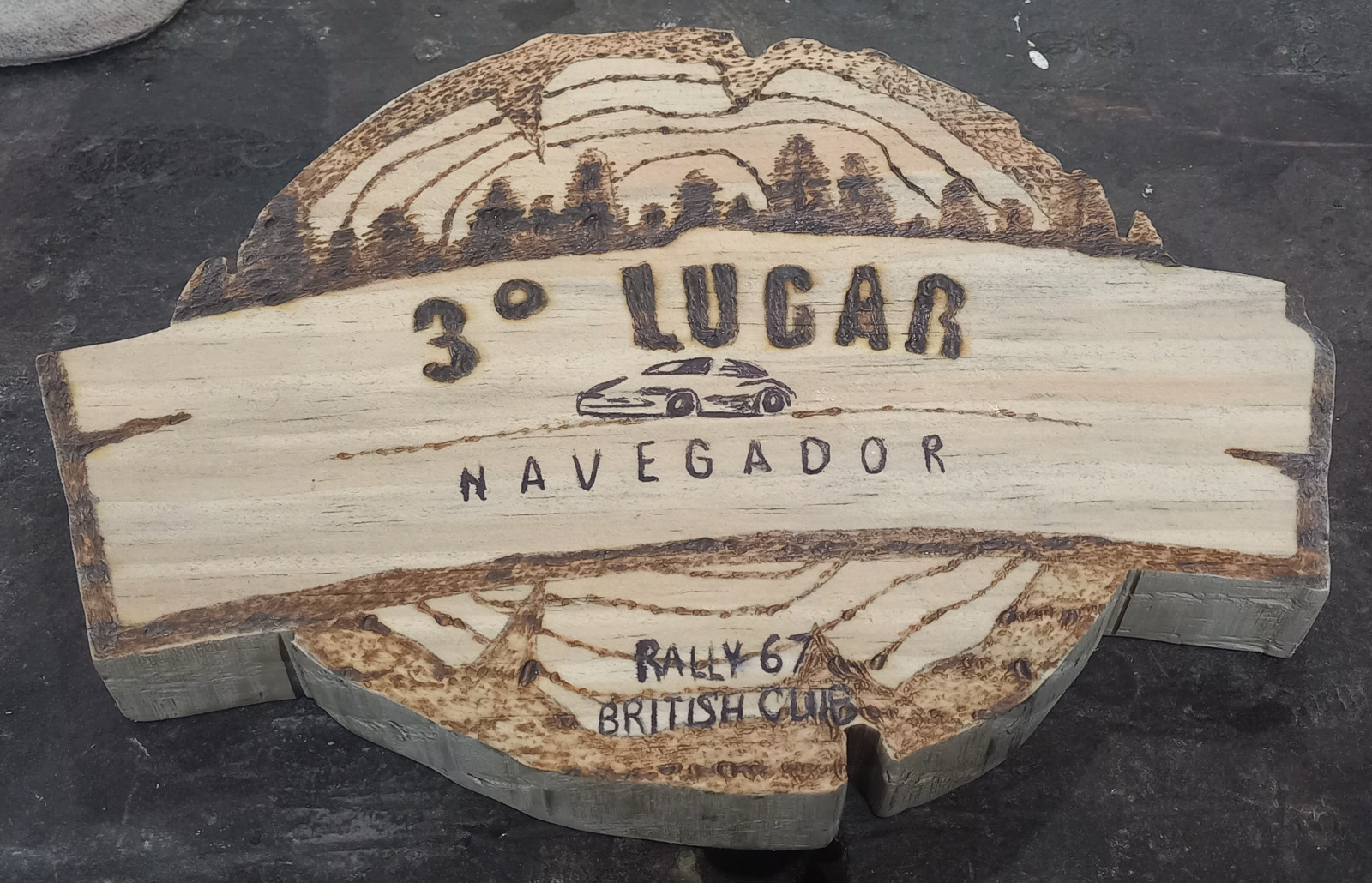 Troféu em madeira maciça pirografado à mão com paisagem de montanhas, carro de rally e a inscrição "3º Lugar Navegador, Rally 67 British Club", com verniz marítimo auto brilho