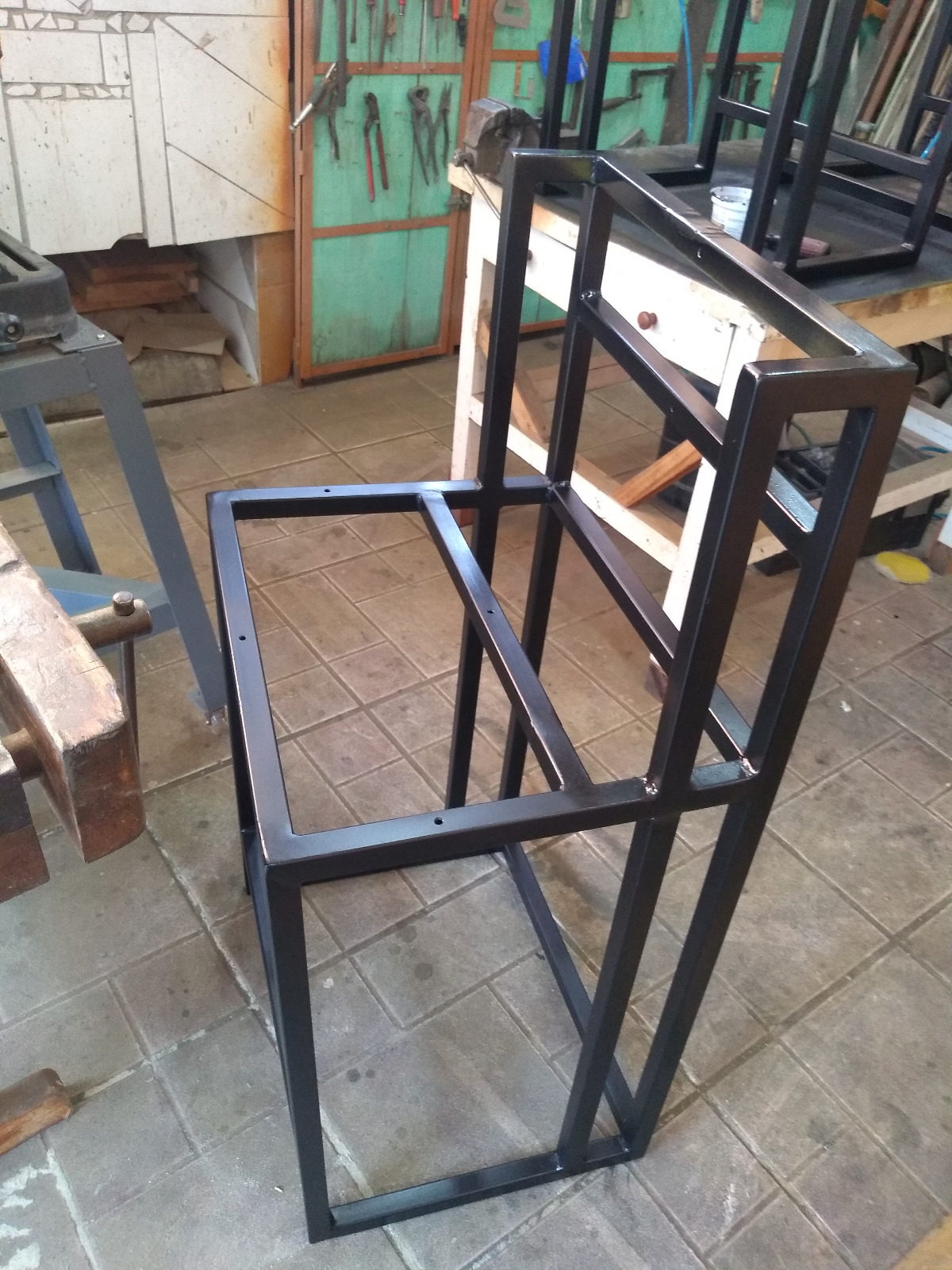 Estrutura de ferro tubular pintada de preto para cadeira alta, apoiada no piso da oficina de solda