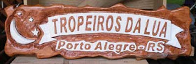 Placa horizontal de cedro branco com lua e estrelas entalhadas e o texto "Tropeiros da Lua, Porto Alegre/RS" em alto e baixo relevo pintado de branco